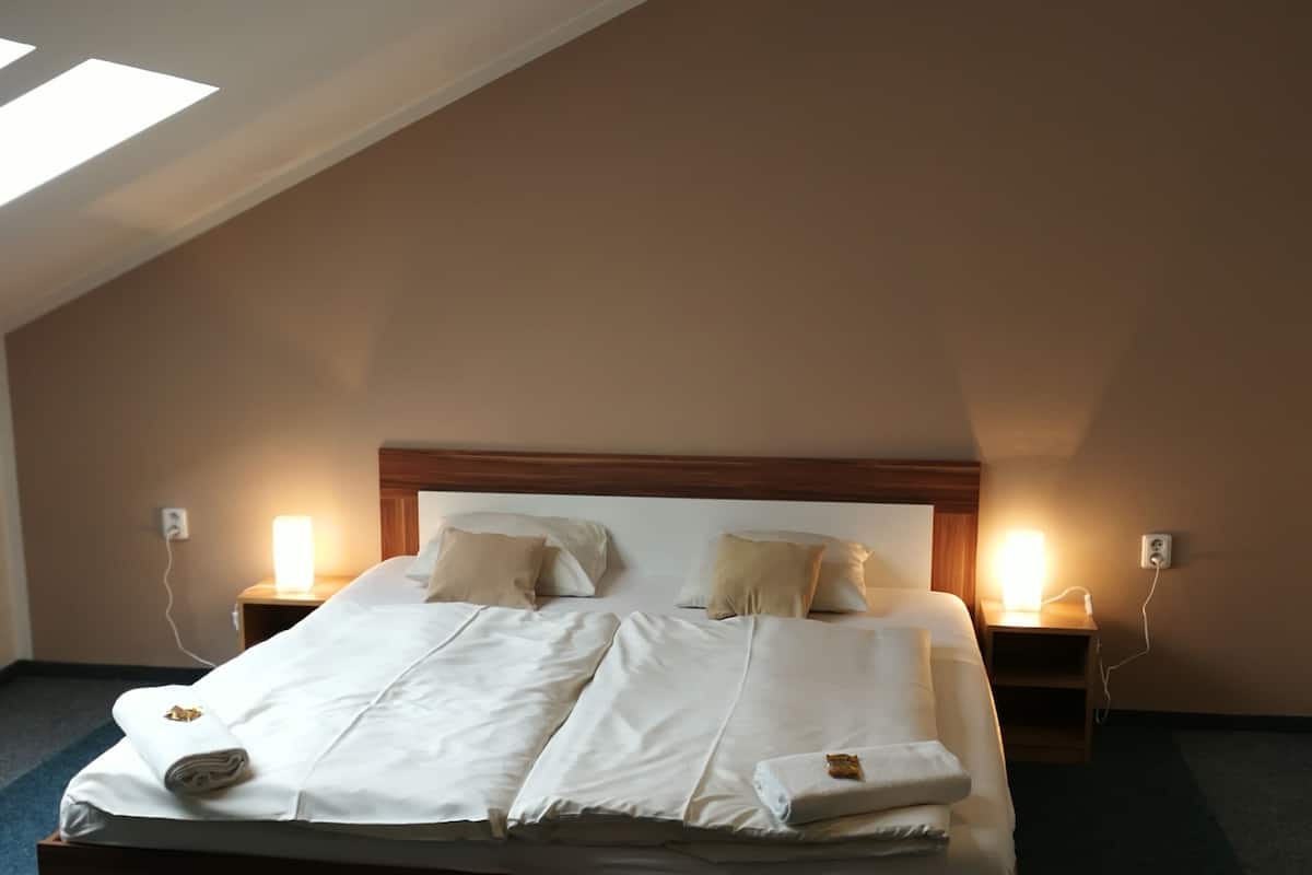 Una cama bien hecha en una habitación con techo inclinado y dos lámparas de noche.