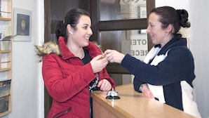 Dos personas en el mostrador de recepción de un hotel, con un mostrador de madera y certificados enmarcados en la pared.
