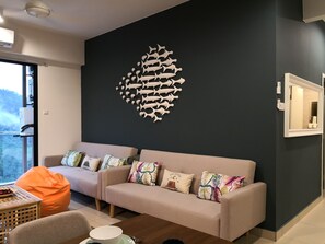 A modern living room with a dark accent wall, a beige sofa with colorful cushions, a wooden coffee table, and a large window offering a view of the outdoors. - Midhill by Cheng (Genting Highlands)