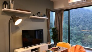 A modern living room with a flat-screen TV, a floor lamp, a bean bag chair, and a large window with a view of a forest. - Midhill by Cheng (Genting Highlands)