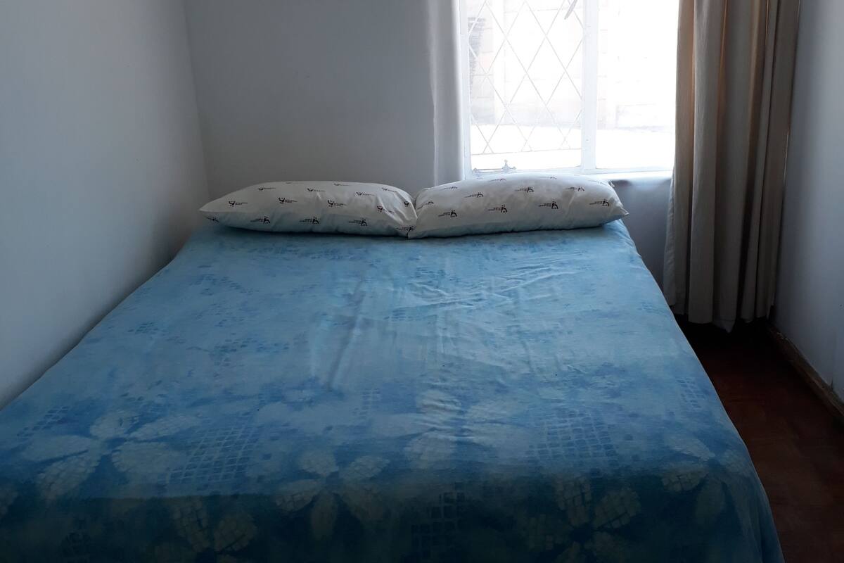 A room with a bed, a window with curtains, and a framed picture on the wall.