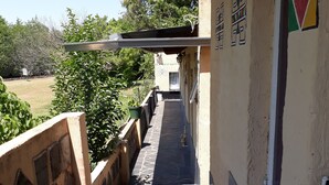 Um corredor exterior com piso de pedra, oferecendo vista para um jardim e árvores.
