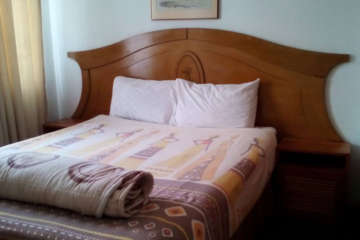 A neatly made bed with a patterned bedspread and a rolled blanket.