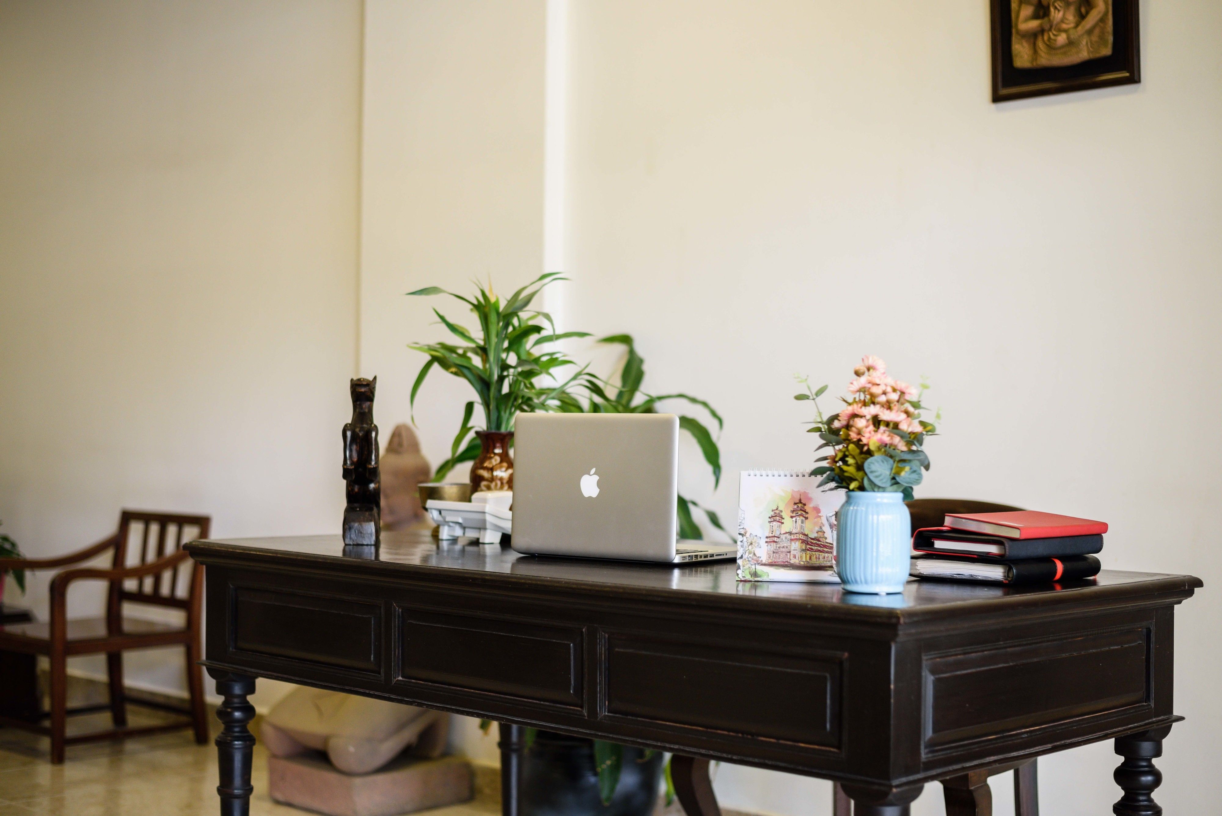 Ein Holztisch mit einem Laptop, einer Blumenvase und einem gerahmten Bild an der Wand.