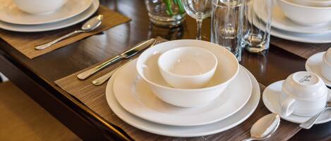 A table set with white dishes, glasses, and cutlery, accompanied by a vase of white flowers.