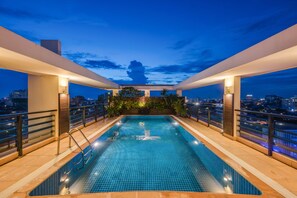 A rooftop swimming pool with a city view at dusk. - City View Apartment (Phnom Penh)