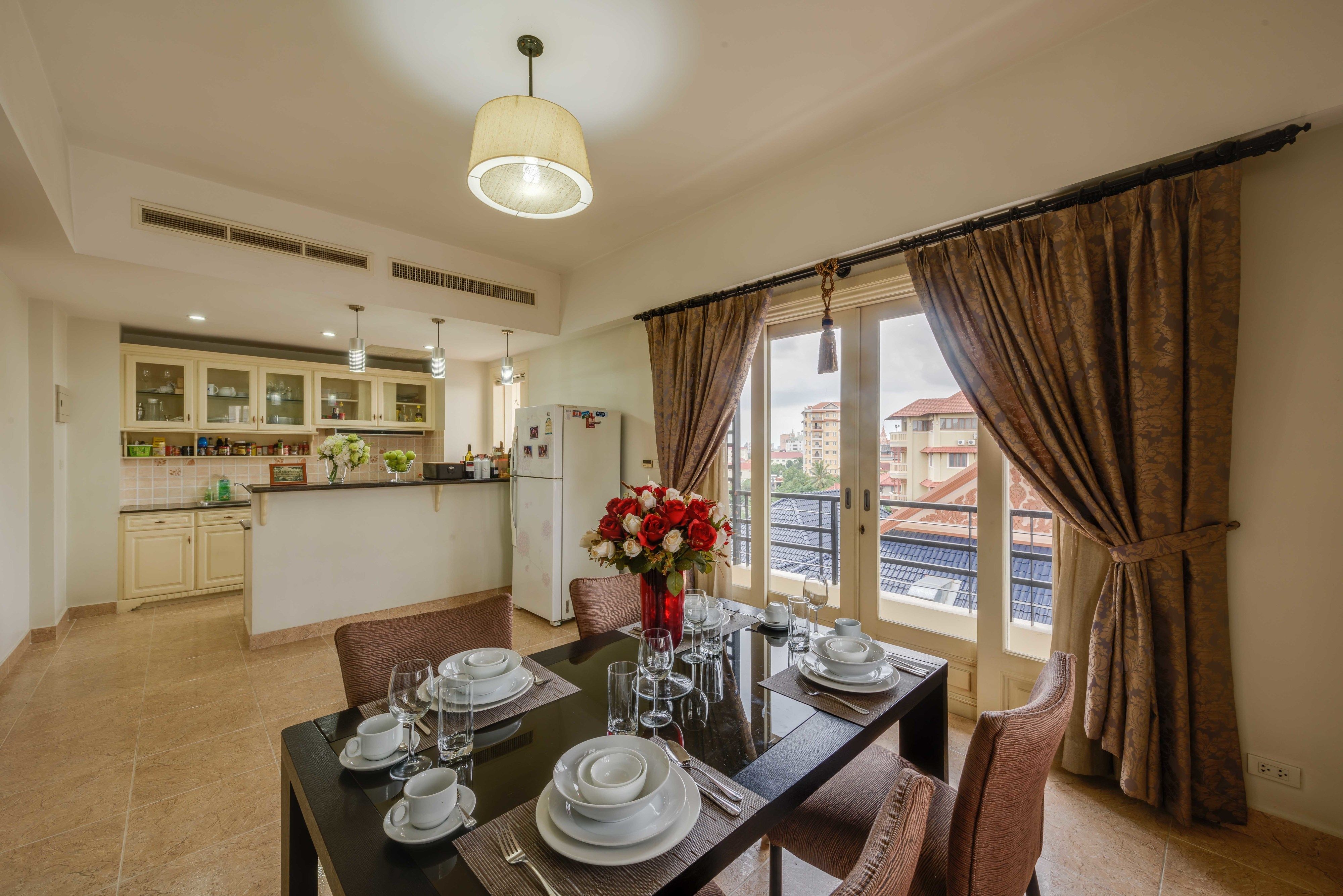 A dining area with a table set for four, a vase with flowers, and a view of the city through large windows.