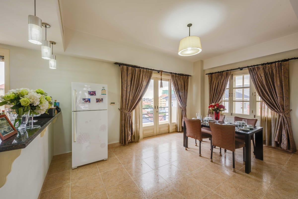 A kitchen with a refrigerator, dining table, chairs, and a hanging light fixture.