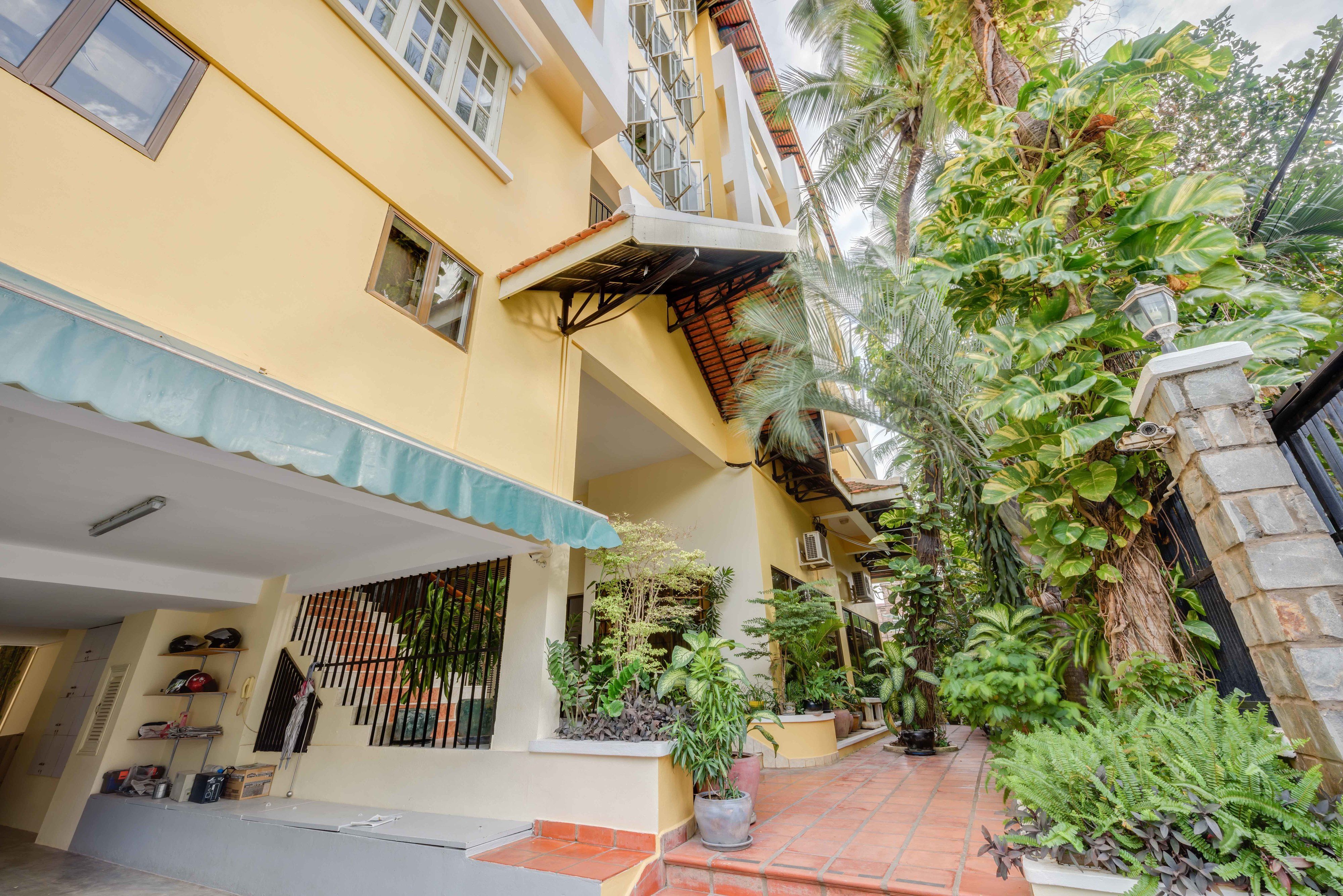 A yellow building with a covered entrance, potted plants, and a staircase leading to an upper level.