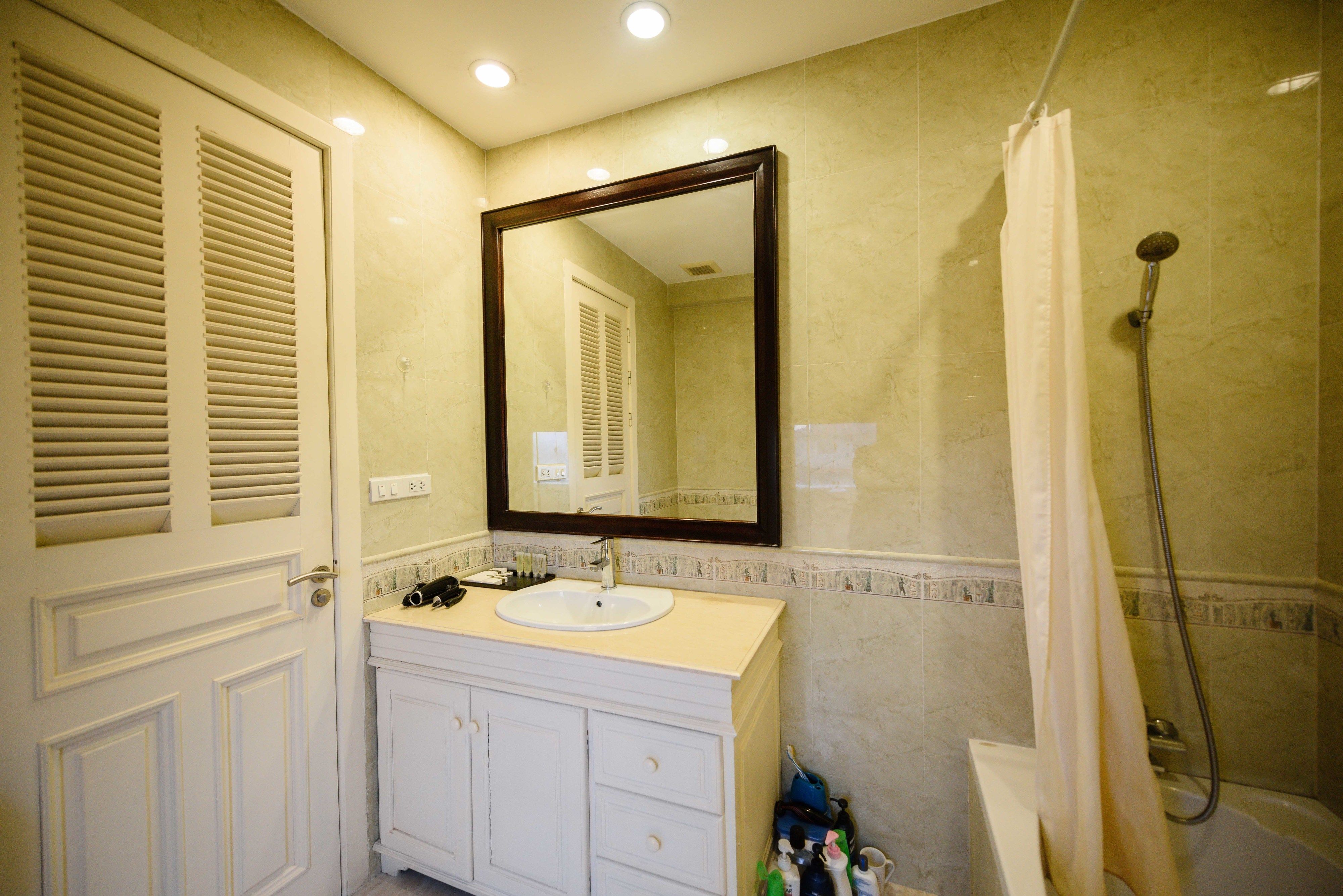 A bathroom with a white vanity, a large mirror, a shower, and a door with louvered panels.