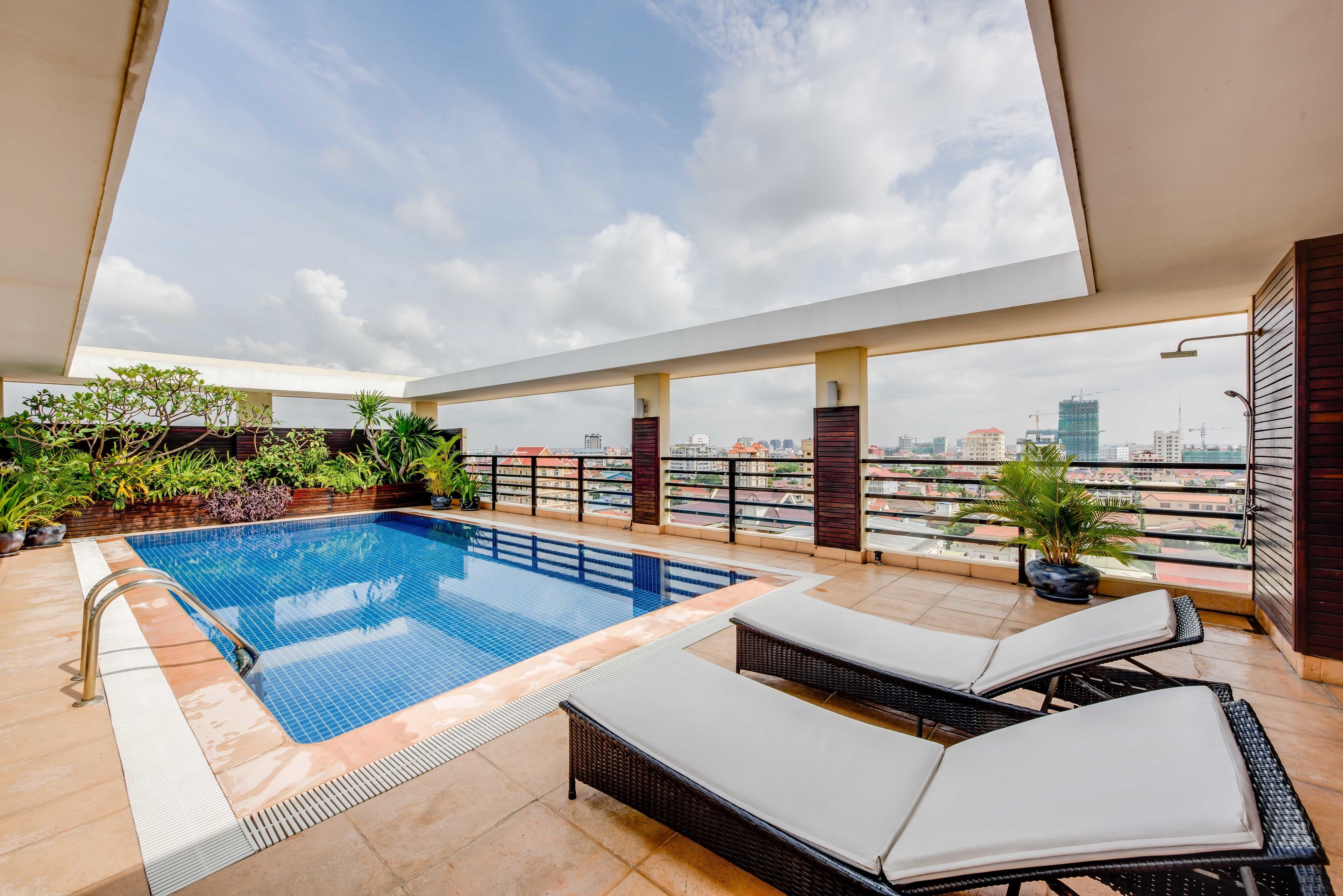 Una piscina en la azotea con sillones de descanso, vistas panorámicas de la ciudad y plantas en macetas.