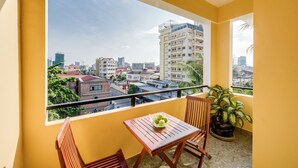 Un balcón con mesa y sillas, una planta en maceta y vista de la ciudad.