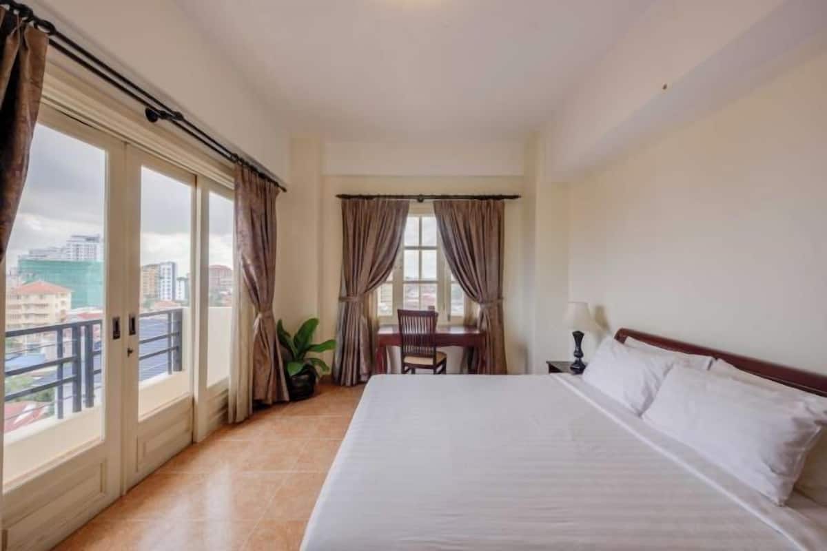 A hotel room with a large bed, a desk, and a view of the city.