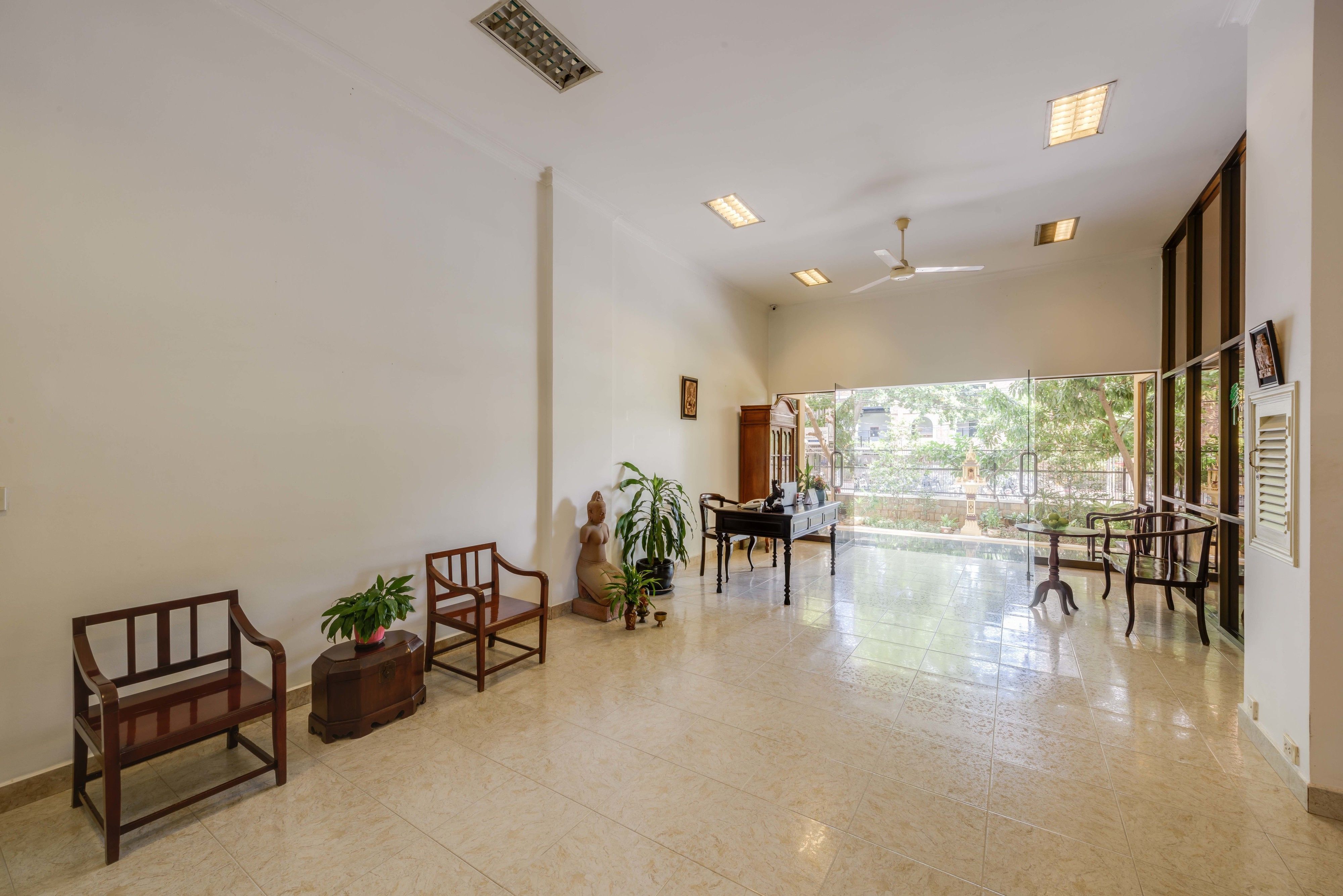 A spacious room with a high ceiling, recessed lighting, a ceiling fan, a large window, and a view of greenery outside.