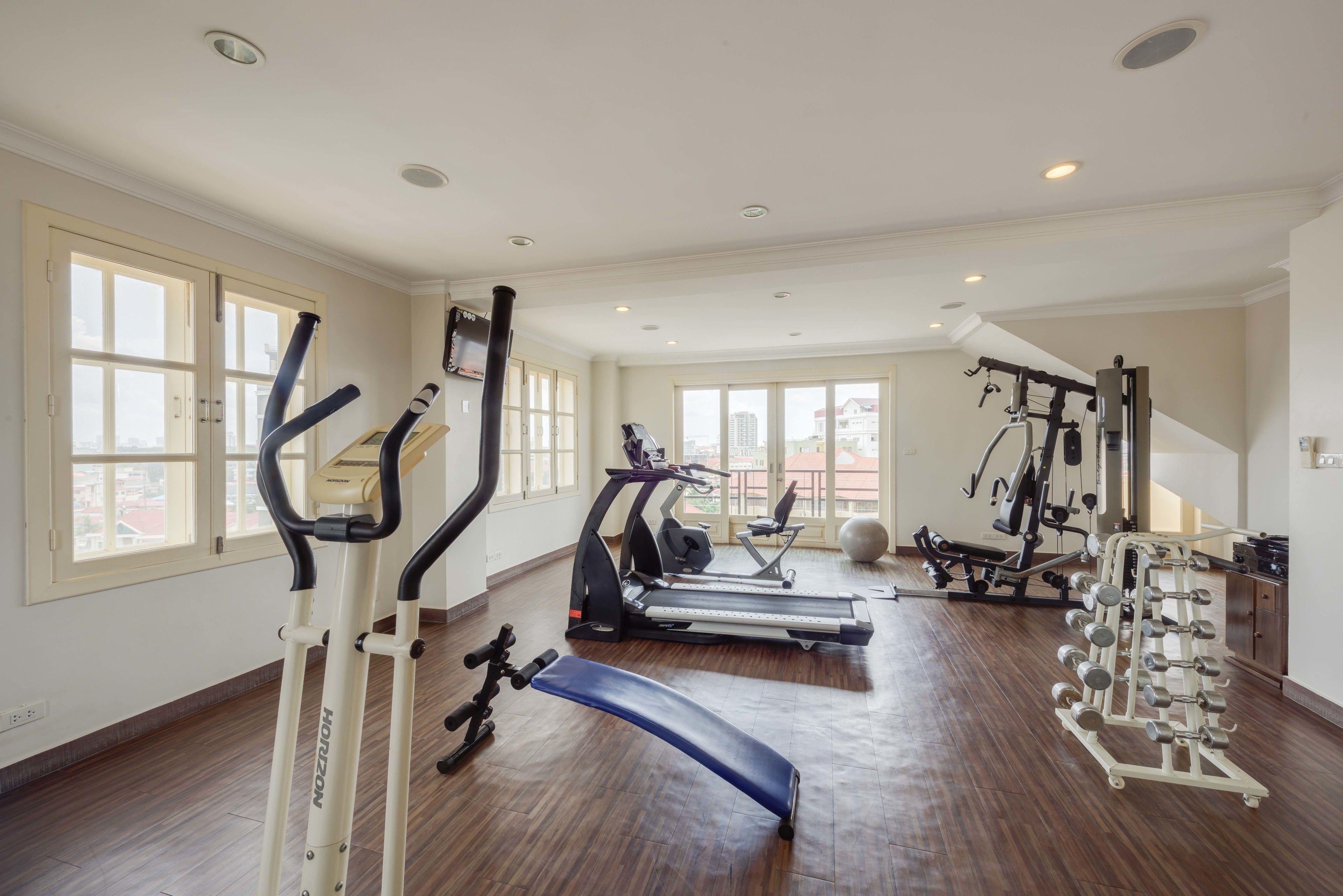 A spacious gym with treadmills, elliptical machines, a bench, and a weight rack.