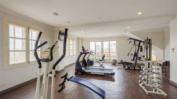 A spacious gym with treadmills, elliptical machines, a bench, and a weight rack.