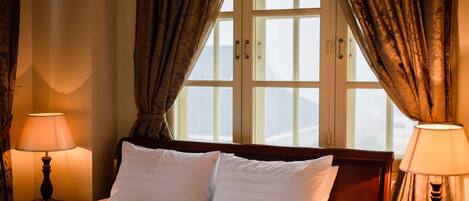 A hotel room with a bed, two bedside lamps, and a window with curtains.