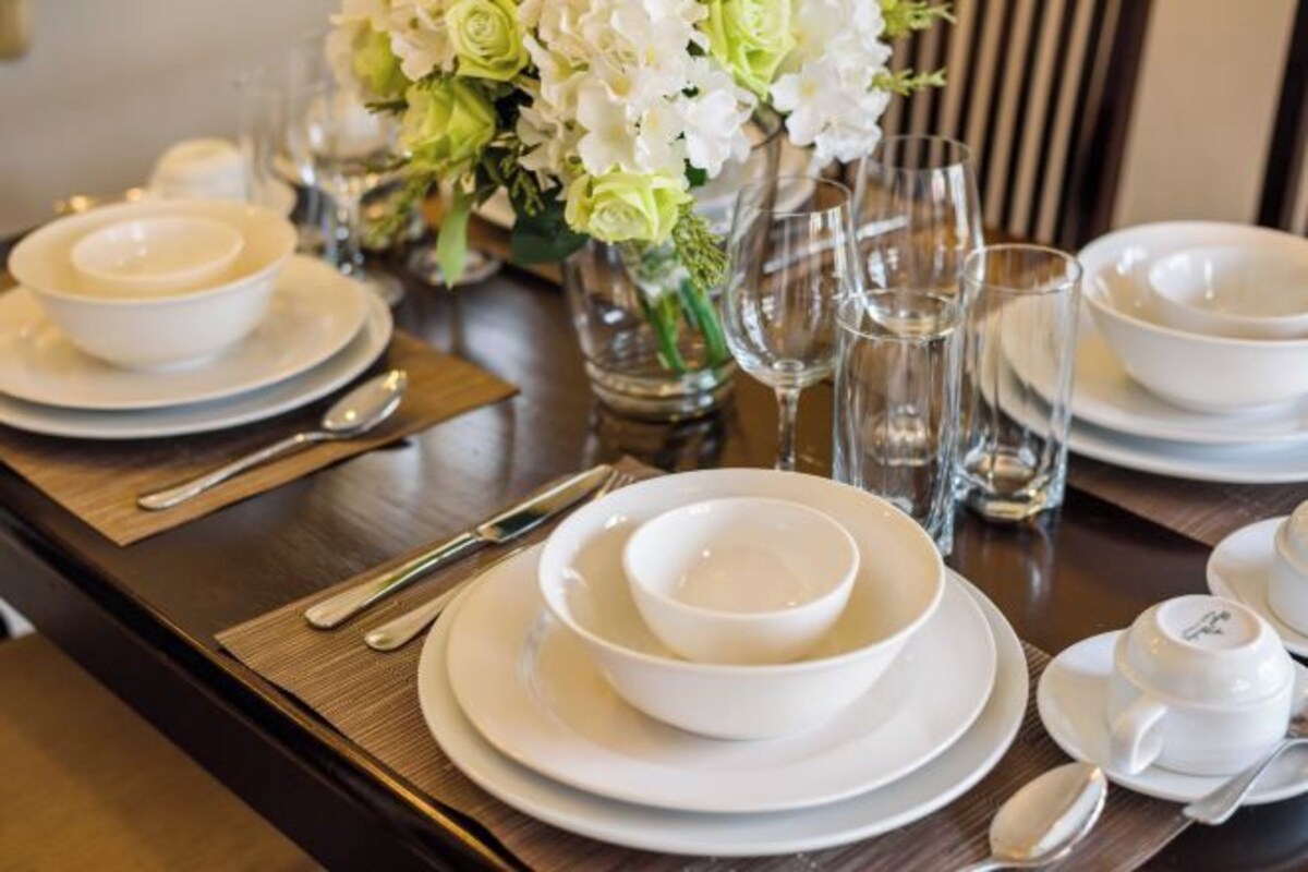 A table set with white dinnerware, including bowls and plates, and a vase with flowers.
