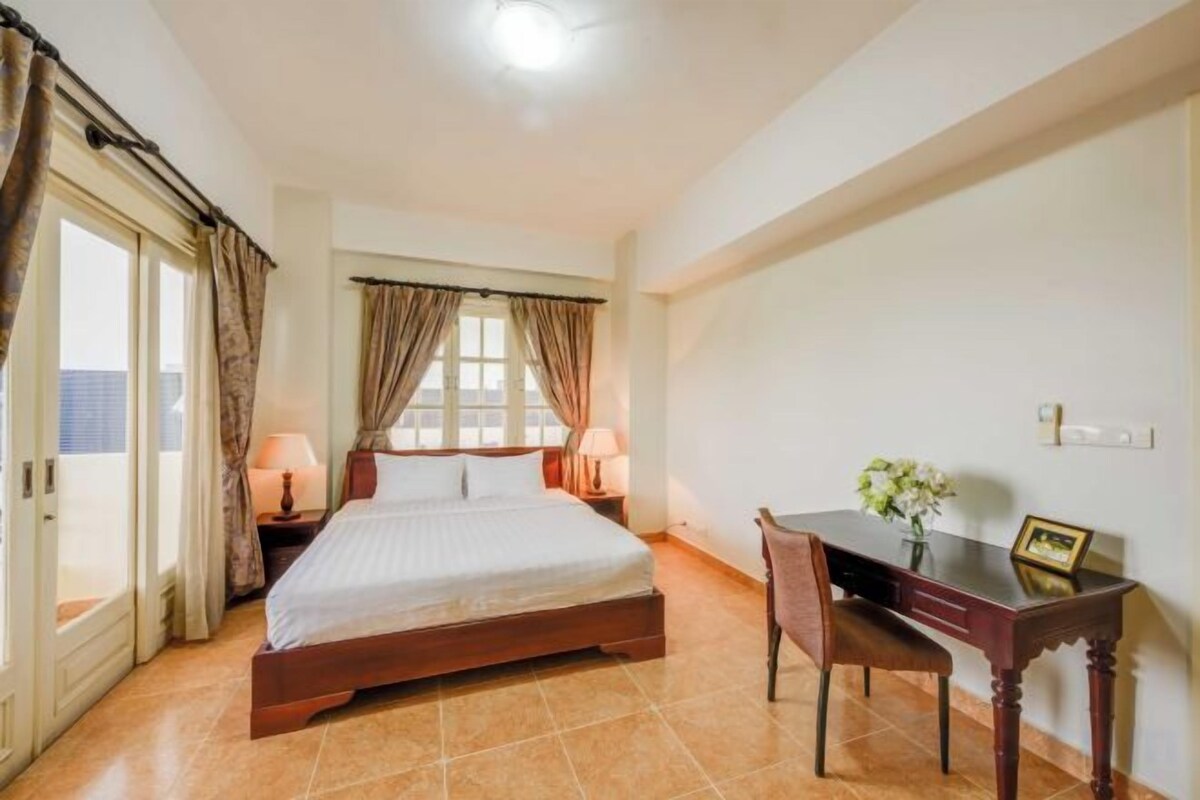 A bedroom with a bed, bedside tables, a desk, and a chair.