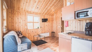 A compact wooden cabin with a kitchenette, a small dining area, and a cozy sleeping space. - Lindarbrekka (Djupivogur)