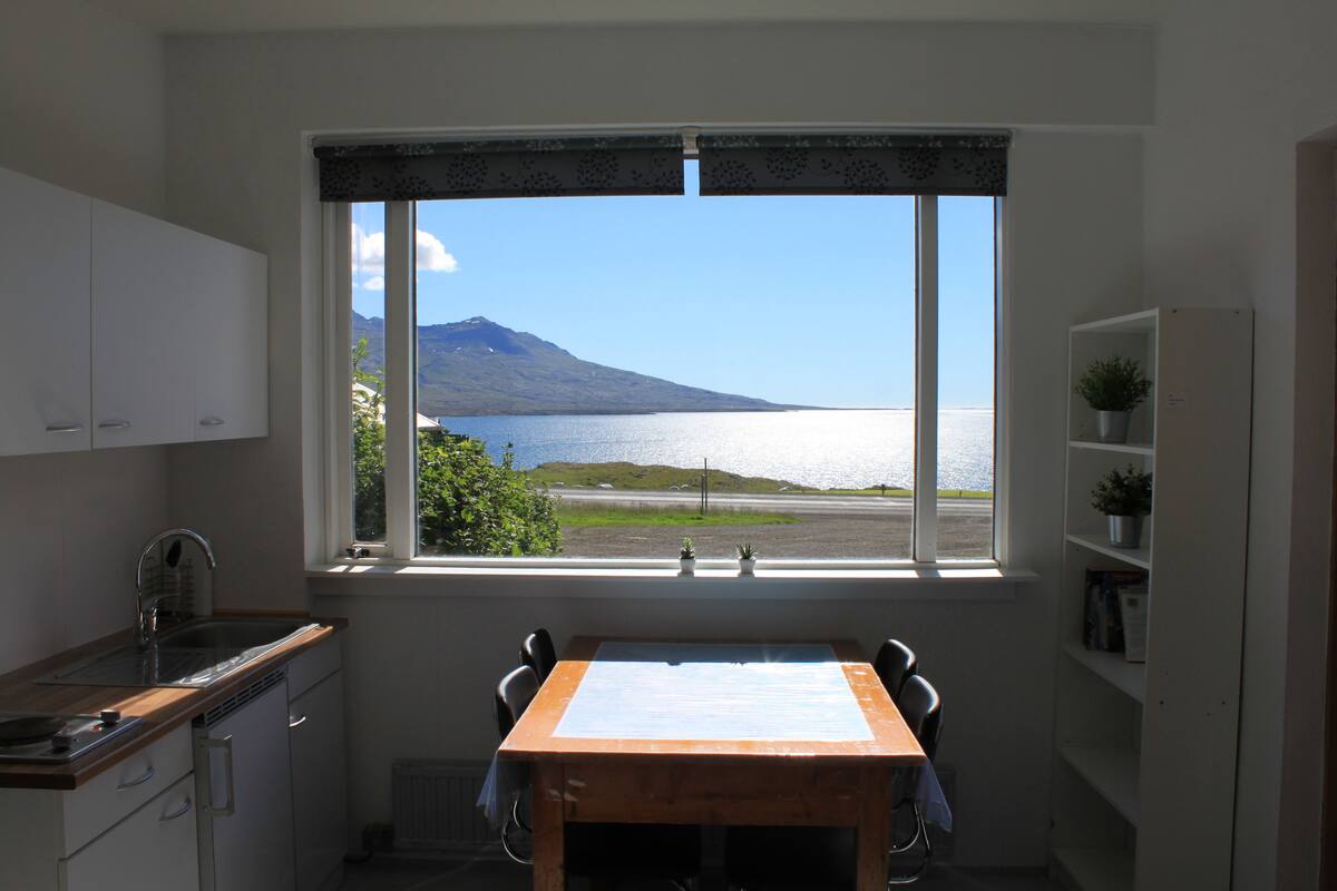 A kitchen with a view of a lake and a mountain, a dining table, and white cabinets.