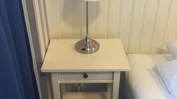 Une table de chevet blanche, avec une lampe, un tiroir et une petite étagère.