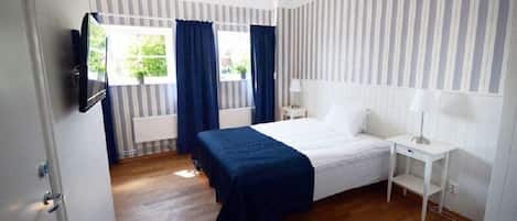 A bedroom with a bed, a bedside table, a lamp, a TV mounted on the wall, and a window with curtains.