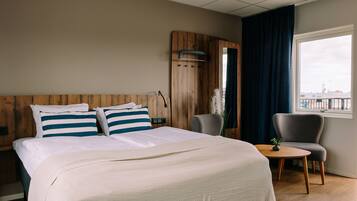 A hotel room with a large bed, a small table, a chair, and a window with a view.