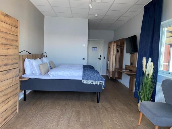 Une chambre moderne avec un lit, un mur recouvert de panneaux en bois, un téléviseur et une fenêtre avec des rideaux.