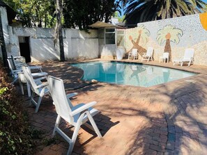 Une piscine bordée de chaises longues blanches et agrémentée d’un mur en mosaïque.