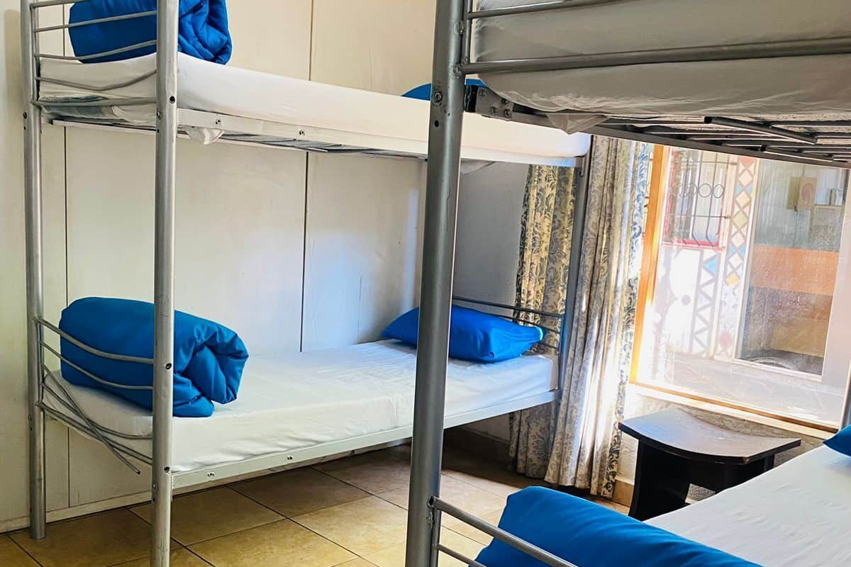 Ein Schlafsaalzimmer mit Etagenbetten, einem Fenster mit Vorhängen und einem Fliesenboden.