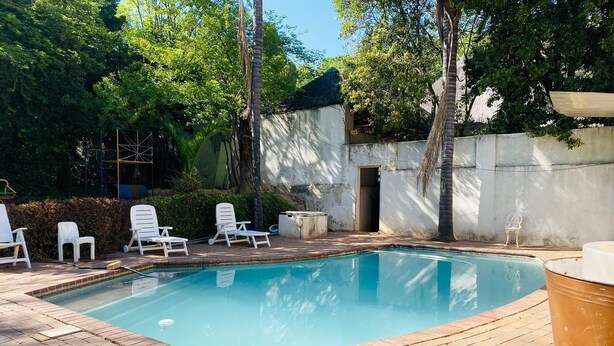 Une piscine rectangulaire bordée de briques, entourée de chaises longues blanches et d’un mur en béton.