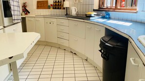 Une cuisine avec des meubles blancs, un sol carrelé, une cuisinière et une fenêtre avec des barreaux.