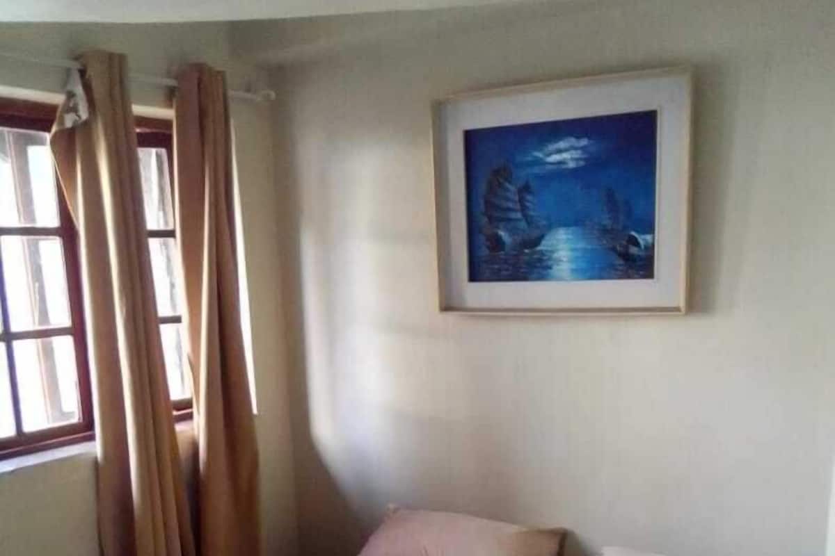 Ein Schlafzimmer mit einem Bett, Vorhängen, einem Fenster und einem gerahmten Bild an der Wand.