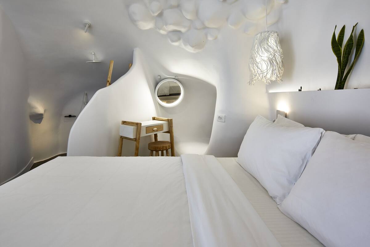 A modern bedroom with a large bed, a round mirror, a desk, and a hanging light fixture.