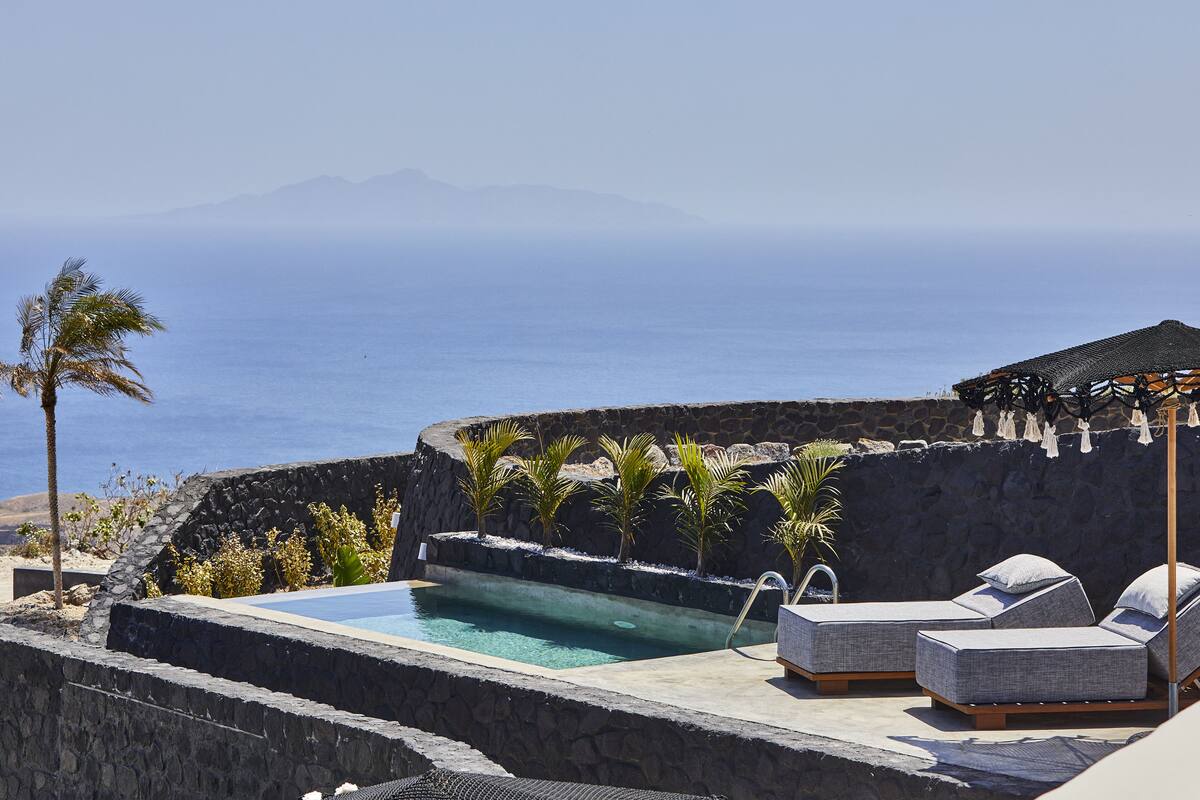 A pool area with lounge chairs, a stone wall, and a view of the ocean.
