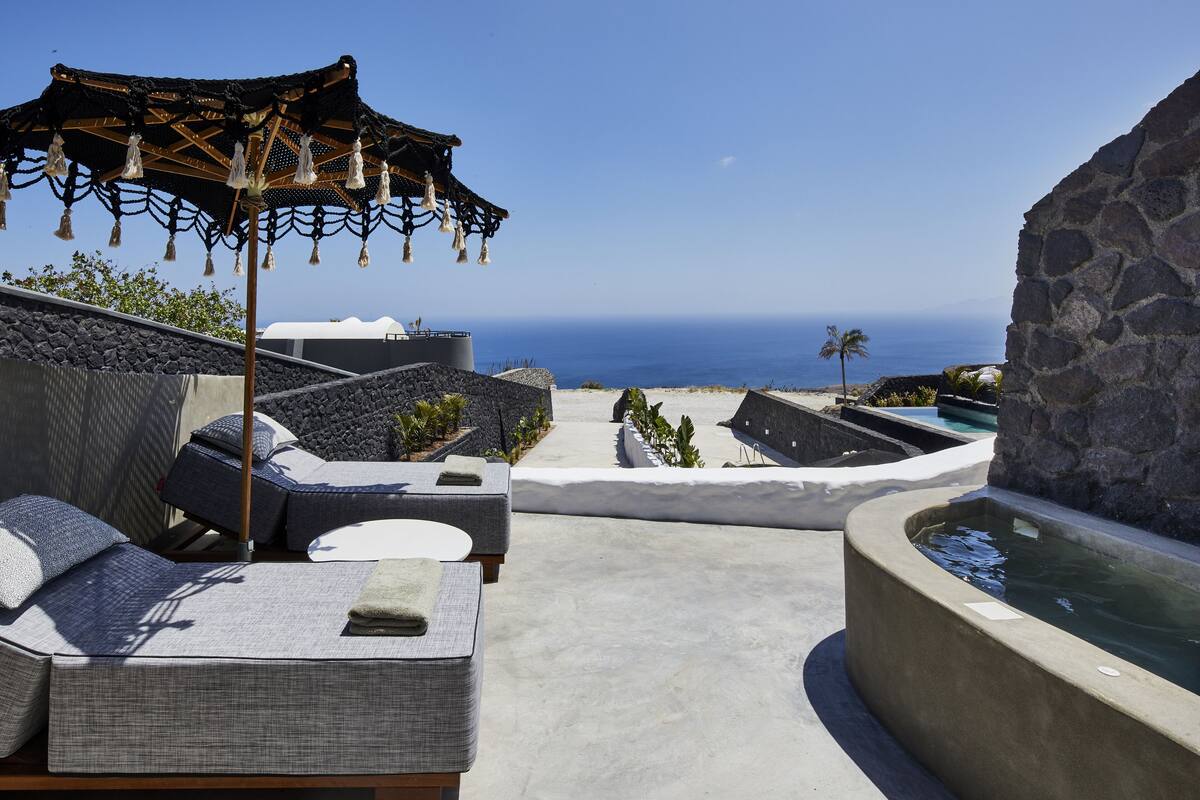 A seaside terrace with outdoor seating, a water feature, and a view of the ocean.