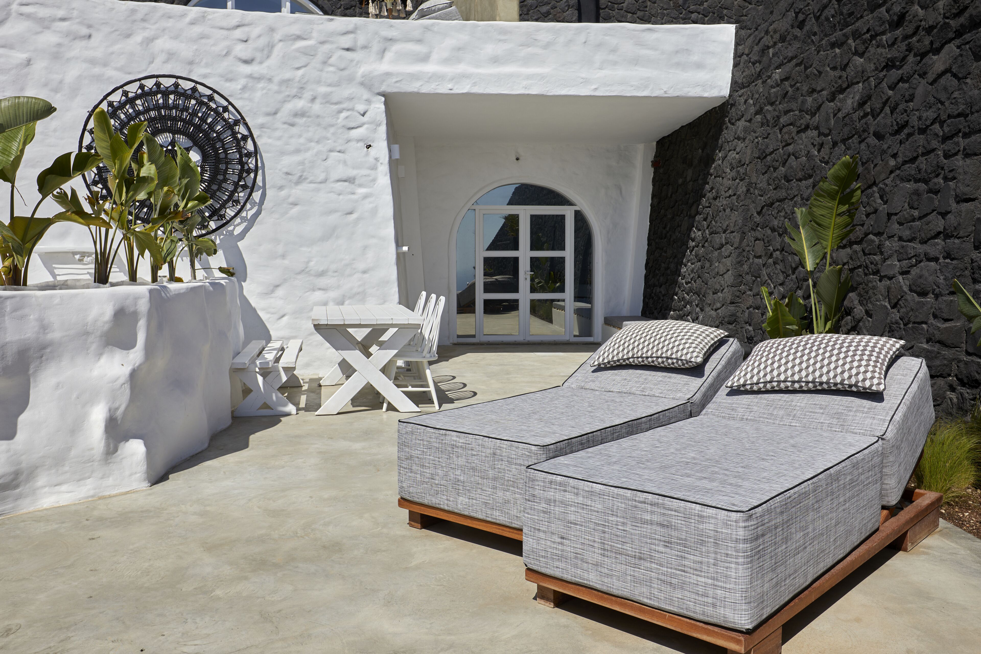 A modern outdoor seating area with two cushioned lounge chairs, a white table, and chairs.