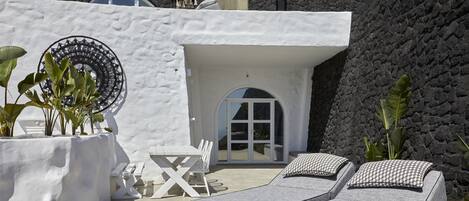 A modern outdoor seating area with two cushioned lounge chairs, a white table, and chairs.