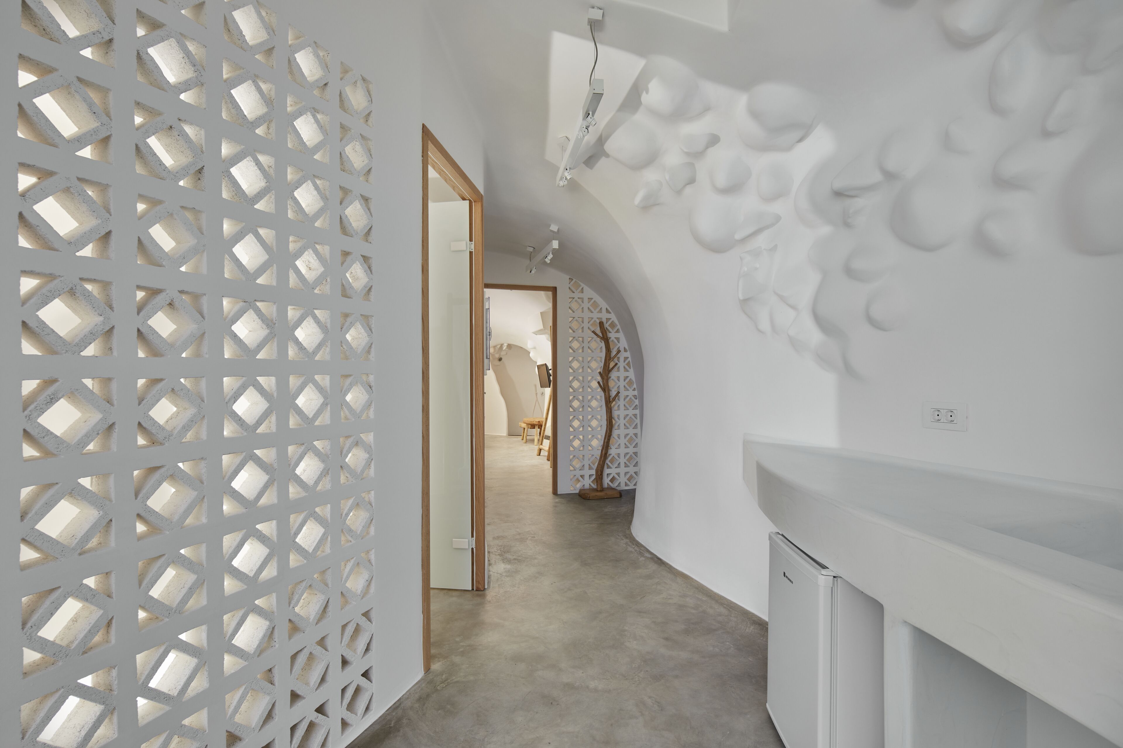 Un intérieur moderne avec un motif géométrique sur un mur, un couloir menant à une pièce, et une esthétique minimaliste.