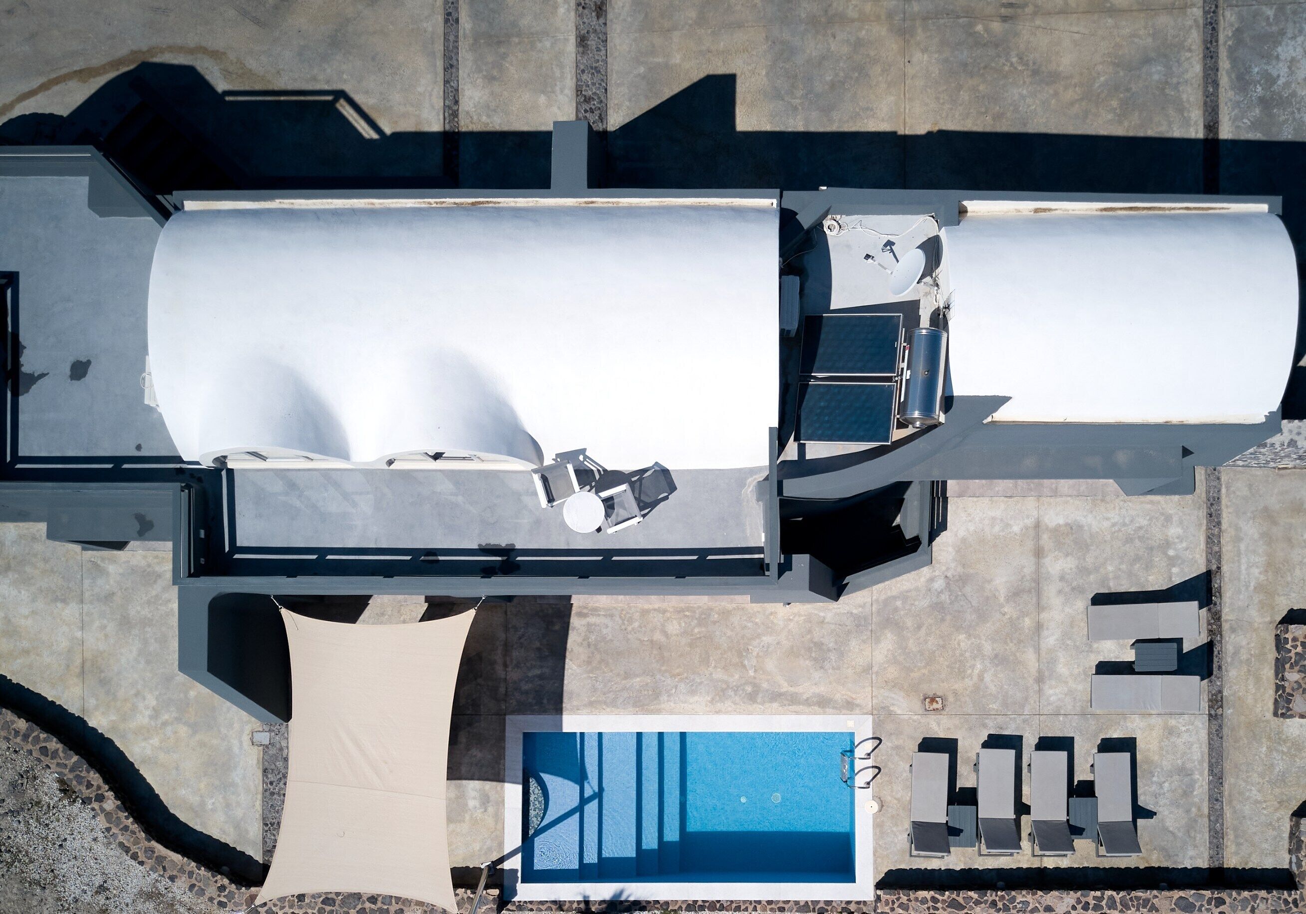 Vista aérea de uma área de piscina com piscina retangular, espreguiçadeiras e um espaço de estar coberto.