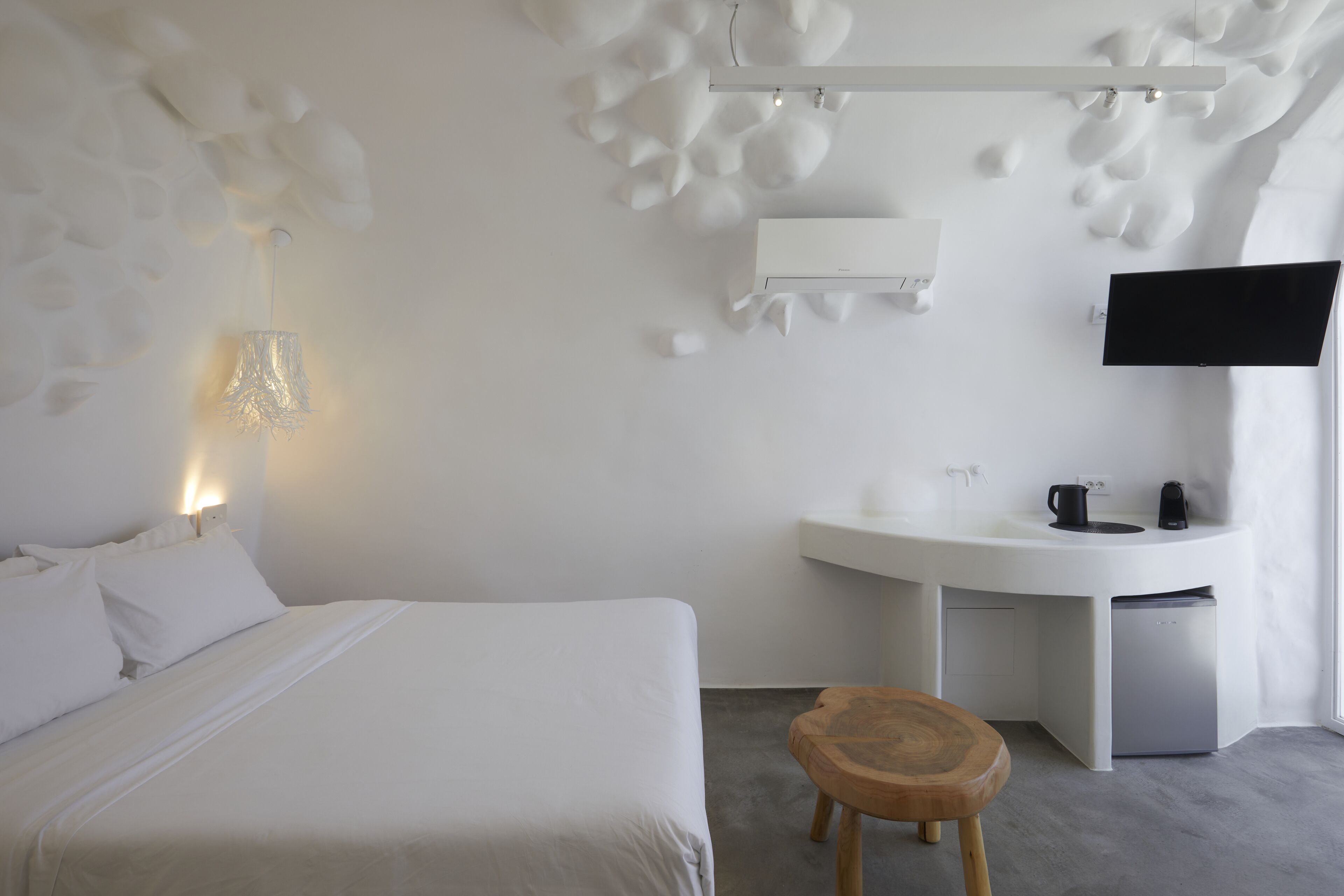 A modern hotel room with a bed, a desk, a flat-screen TV, and a small stool.