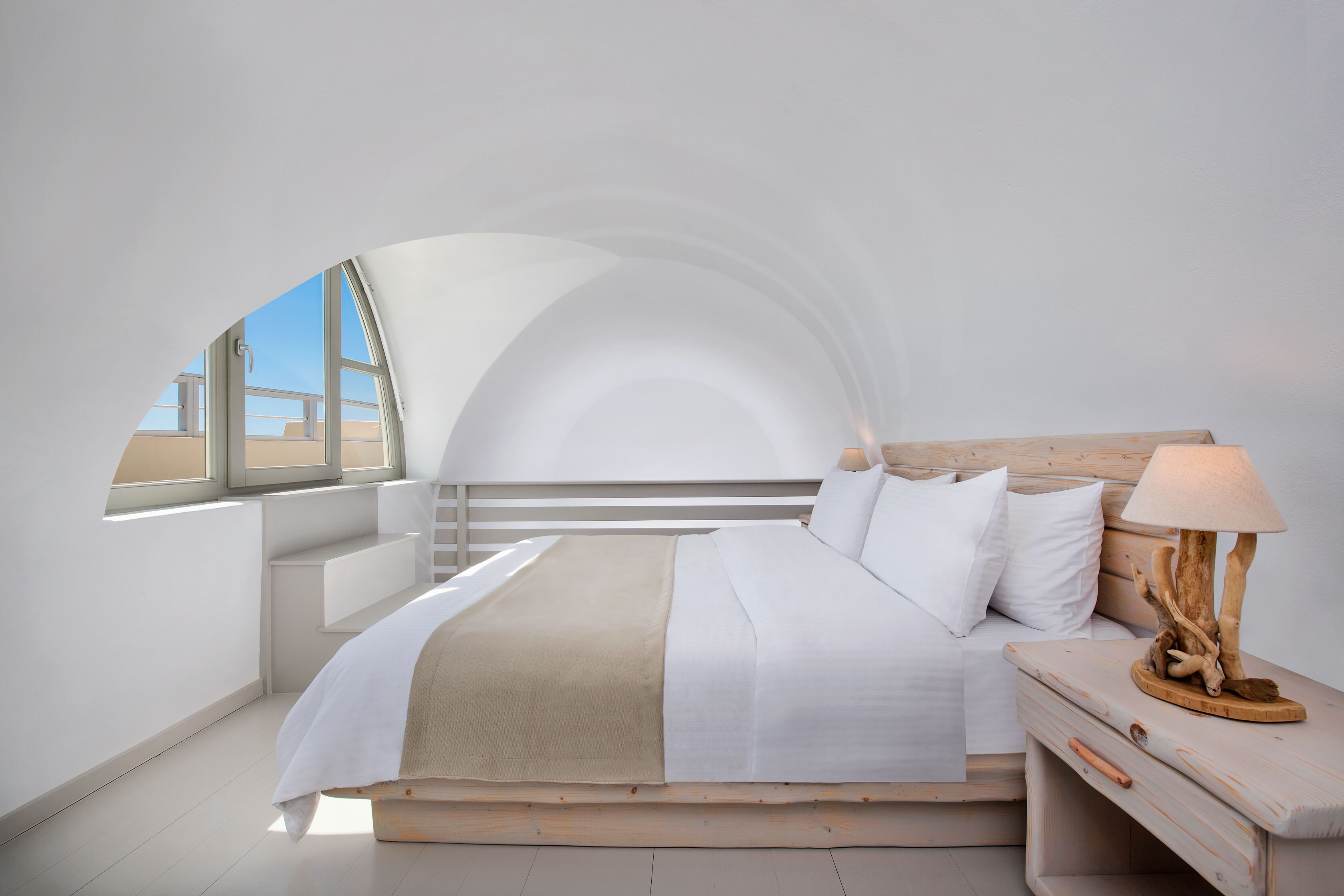 A modern bedroom with a large bed, a wooden nightstand, and a window with a view of a building.