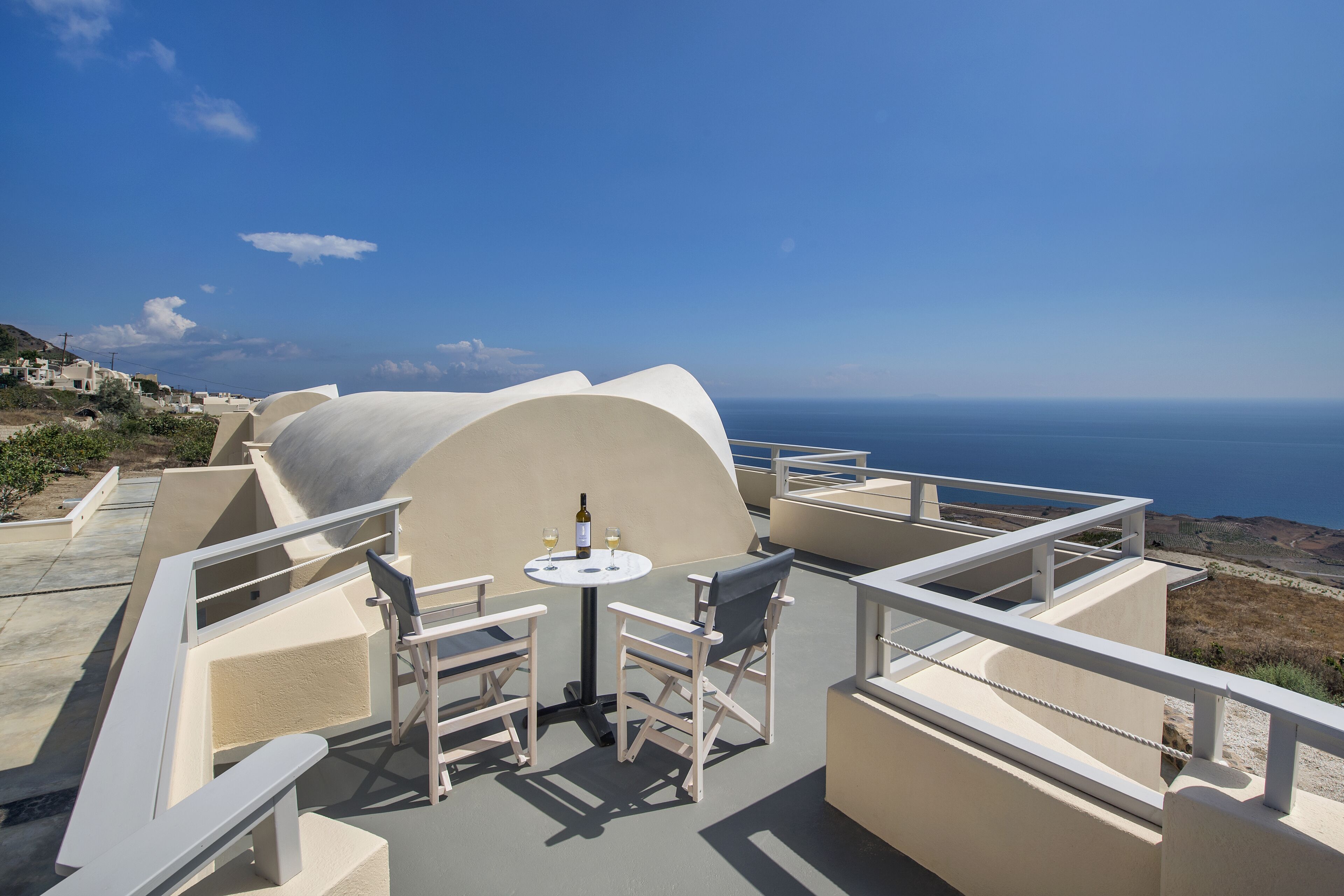 Una terraza con mobiliario blanco y una mesa, con vistas a un paisaje costero.