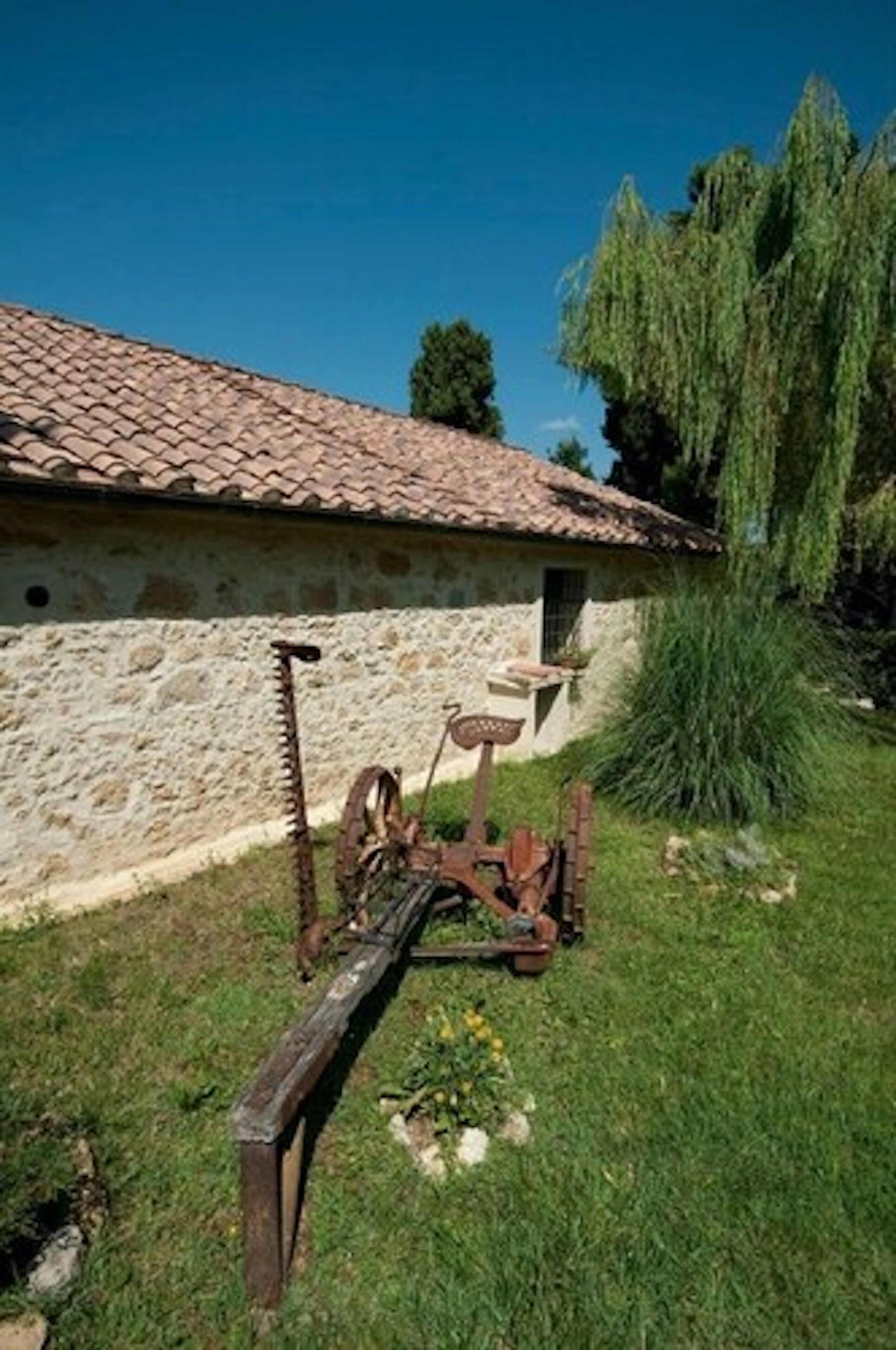Un bâtiment rustique en pierre, avec un toit de tuiles, un banc en bois et un outil en métal rouillé au premier plan.