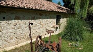Un bâtiment rustique en pierre, avec un toit de tuiles, un banc en bois et un outil en métal rouillé au premier plan.