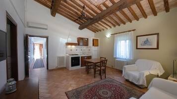 A spacious living area with a wooden ceiling, a dining table with chairs, a covered sofa, and a patterned rug.