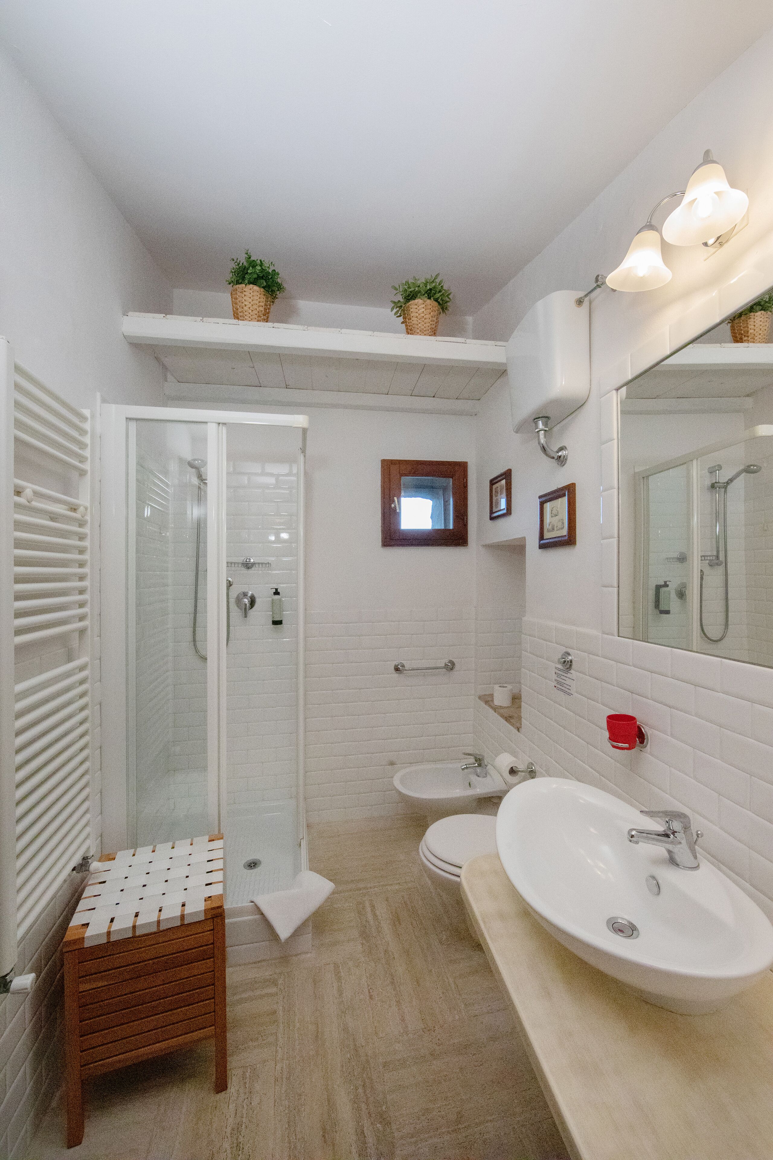 Un baño moderno con cabina de ducha de vidrio, un taburete de madera, un lavamanos grande y un espejo con luz.