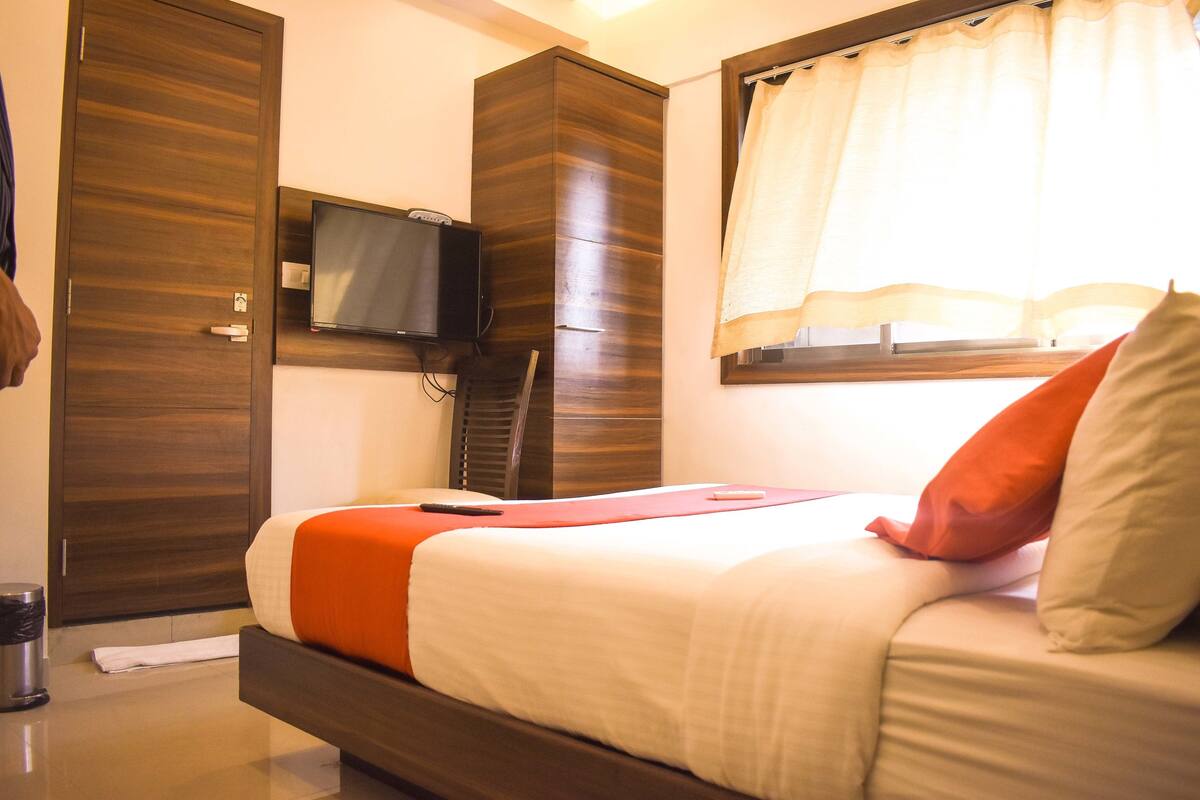 Une chambre d’hôtel avec un lit, un téléviseur fixé au mur et une fenêtre avec des rideaux.