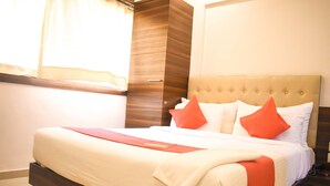 A neatly made bed with a red and white bedspread, a wooden headboard, and a window with sheer curtains. - Hotel Mumbai International (Mumbai)